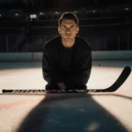 Jesse Kortuem sits on hockey ice with stick across his legs showing determination and self-acceptance
