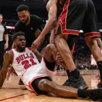 Jimmy Butler lies on the court clutching his knee injury with teammates helping him up and Heat bench watching in shock