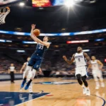 Luka Doncic sinking three-pointer over defender with neon city lights reflecting on court