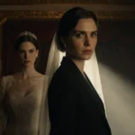 Maggie Gyllenhaal stands confidently beside The Bride character with warm theater lighting casting long shadows and hinting a