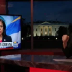Rep. Marjorie Taylor Greene speaking at desk with TV screen showing Maduro Capture graphic and White House in background