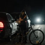 Mother comforting child beside damaged bicycle with hazard lights flashing and police flashlight in darkness