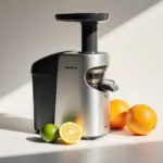 Nama J3 cold press juicer stands vertically with fresh citrus fruits arranged nearby showing sleek compact design