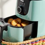 Ninja Crispi Portable Glass Air Fryer resting on woven basket with golden snacks and pastel colors highlighted by soft light