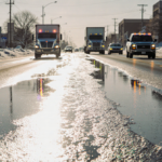 Main road glistening with ice and slush cars halted with flashing hazard lights under winter sun