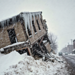 Snow blankets collapsed building with icicles hanging and snowdrifts piling.