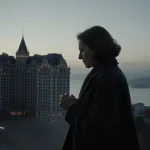 Woman walking toward Fairmont Hotel with long coat and clasped hands against misty Bay and dawn sky