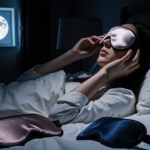 Person gently placing a silk sleep mask over their eyes with a moonlit window glowing and plush pillows in night scene