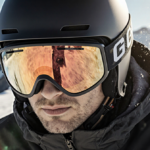 Skier glides down mountain slope with sleek high‑end goggles reflecting warm sun.