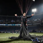 Skydiver standing with arms open shocked with parachute tangled in goalpost netting at stadium lights