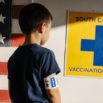 Measles child looking over shoulder toward yellow blue vaccination center sign with arm band against flag background