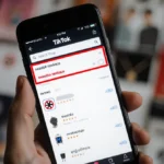 Smartphone shows TikTok Shop search bar with red swastika necklace query and disturbing product hints with blurred items behi