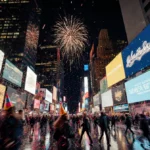 Crowd rushing to catch countdown in Times Square with fireworks lighting wet pavement and neon billboards.