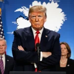 Donald Trump stands sternly at podium with Greenland map and nervous delegation behind
