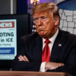 Donald Trump sits at a podium arms crossed as a newspaper headline about the ICE shooting flashes and a map looms behind.