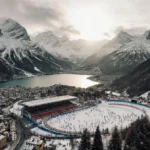 Skier racing down snowy slope with Winter Olympics venue and mountain peaks in background