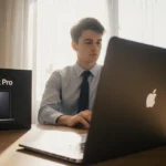 Young professional sitting at desk with MacBook Pro box behind and warm daylight streaming in